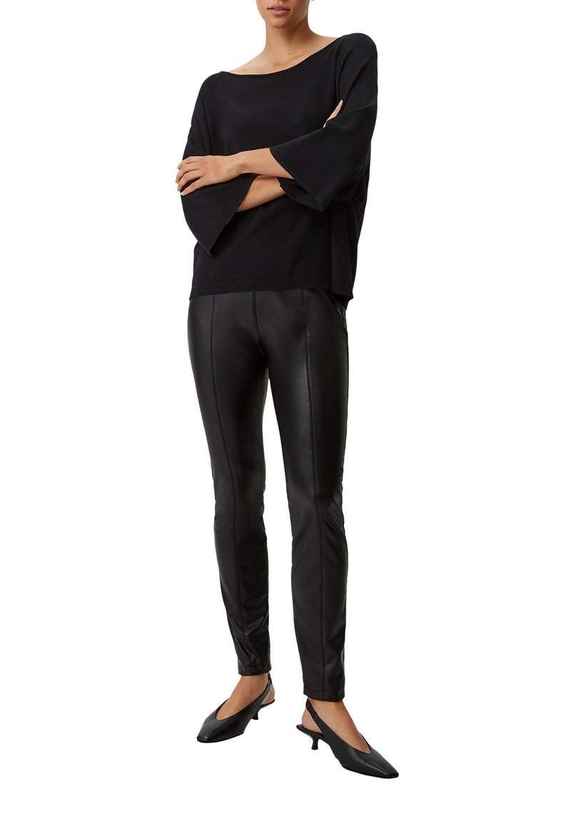 Czarny, oversize sweter z szerokimi rękawami, zestawiony z dopasowanymi spodniami z czarnej sztucznej skóry. Obuwie ma spiczaste noski i fason slingback.