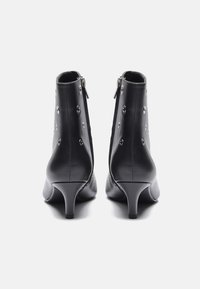 Botas de tobillo de cuero negro con punta afilada, tacón cónico y tachuelas plateadas decorativas a lo largo de los lados. Cierre con cremallera en la parte trasera.