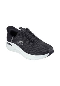 Zapatilla deportiva negra con parte superior de punto texturizado, diseño con cordones, media suela blanca y un logotipo prominente en el costado.