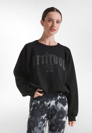 Black sweatshirt with a crew neck, featuring a large graphic "ATTITUDE" in dark gray. Paired with patterned black and gray leggings.
