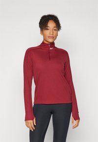 Burgundska majica dugih rukava za sport s polu-zip ovratnikom i Nike logotipom. Ima glatku teksturu i uski kroj.