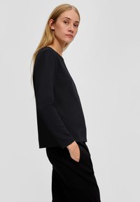 Zwarte textuurtop met lange mouwen, voorzien van een ronde halslijn en een relaxte pasvorm, gecombineerd met zwarte losvallende broek.