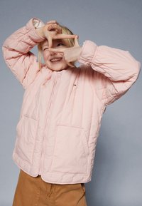 Heled roosa tikandiga jakk, millel on lukuga esiosa ja kaks eesmist taskut. Jakk on varustatud seisva kraega ja elastsete mansettidega mugavaks sobivuseks.