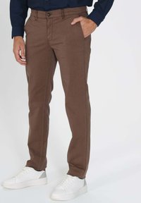 Pantalons en coton marron avec une coupe droite, dotés d'une poche avant et d'une fermeture à un bouton. Associés à des baskets blanches.