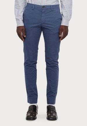 Blauwe katoenen chinos met een slim fit, met een knoopsluiting en riemlussen. Gepaard met donkerbruine loafers en witte sokken.