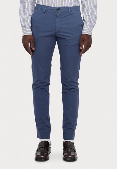 Chino en coton bleu avec une coupe slim, dotés d'une fermeture à bouton et de passants de ceinture. Associés à des mocassins marron foncé et des chaussettes blanches.