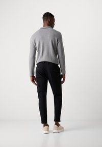 Grijze, lichte gebreide trui met een opstaande kraag, gecombineerd met zwarte tapered broeken met twee achterzakken. Afgemaakt met beige sneakers.