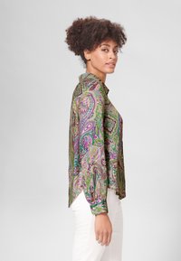Langarmshirt in een levendige groene en paarse paisleyprint, met een kraag en een soepele stof. Zijsplit voor meer bewegingsvrijheid.