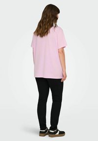 Pink cotton t-shirt with short sleeves, relaxed fit, and a round neckline, paired with black skinny jeans and dark sneakers.