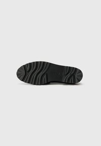 Suela de zapato de goma negra con patrones de agarre texturizados y surcos pronunciados. Presenta un logo de marca sutilmente grabado en la superficie.