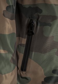 Camouflage fabric with shades of green and brown, featuring a black zipper and matching pull tab. Smooth texture, durable material.