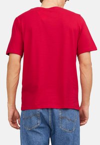 Rød bomulds T-shirt med korte ærmer og rund hals. Bagsiden er simpel, uden mønstre eller detaljer. Bæres med blå jeans.
