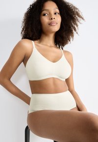 Set di reggiseno senza cuciture in beige chiaro e mutandine a vita alta realizzato in tessuto morbido ed elastico, con una consistenza liscia e un design minimalista.