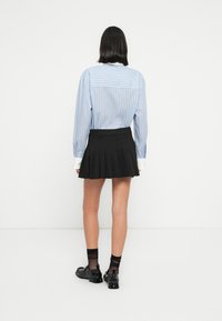 Ανοιχτό μπλ ε ριγέ πουκάμισο με λευκά μανίκια, συνδυασμένο με μαύρη plisέ φούστα. Μαύρα παπούτσια με υφή και διάφανα μαύρα καλσόν.