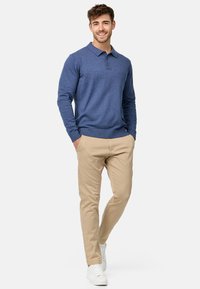 Blå langermet polo skjorte med krage og knapper, paret med beige chinos og hvite sneakers. Glatt tekstur, tilpasset design.