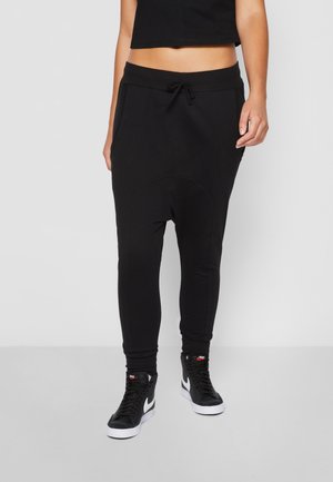 Persona vistiendo pantalones jogger negros de tiro bajo con cintura ajustable y zapatillas Nike de caña alta negras con el símbolo Swoosh blanco.