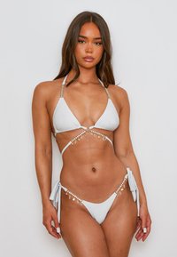 Witte bikini met een gematteerde afwerking. Beschikt over driehoekige cups, gouden hardware en decoratieve charms langs de bandjes en zijkanten.
