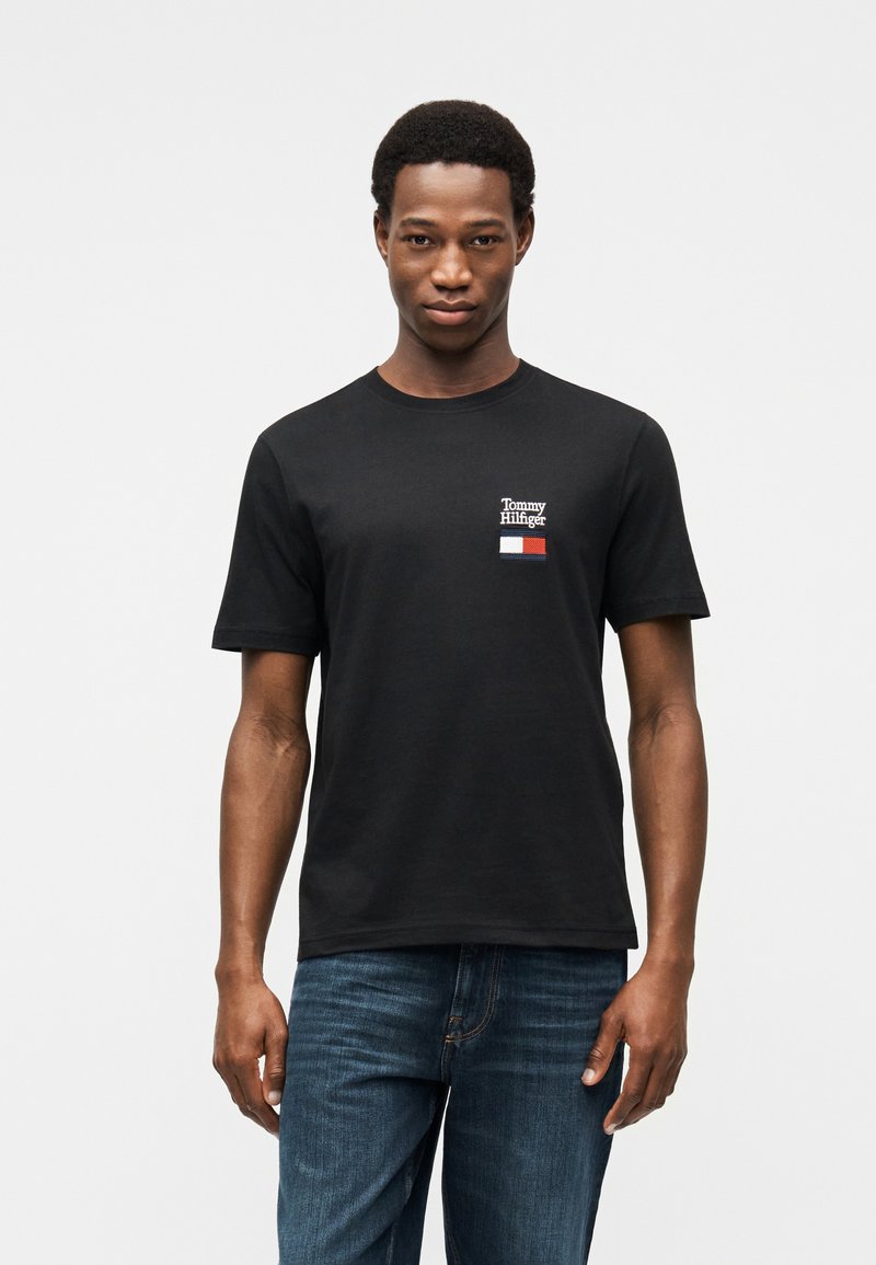 Μαύρο βαμβακερό μπλουζάκι με μικρό κεντημένο λογότυπο σε κόκκινες, λευκές και μπλε αποχρώσεις. Κοντά μανίκια και λαιμόκοψη παντελονιού.