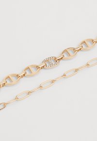 Collana in oro con catena che presenta due design intrecciati: uno con accenti di lettere e una chiusura impreziosita da cristalli, l'altro una semplice maglia ovale.