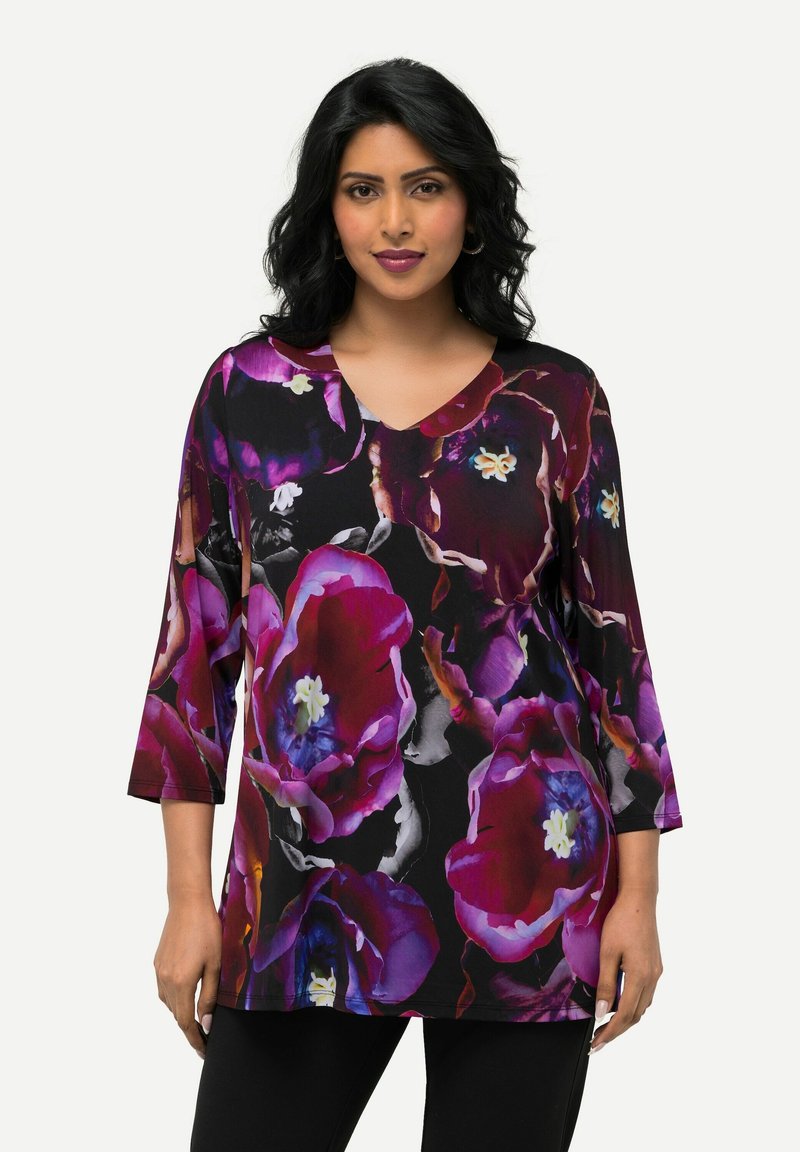 Blühende Tunika mit schwarzem Hintergrund und großen lila und rosa Blumenmustern, V-Ausschnitt und Dreiviertelärmeln. Weicher Stoff.