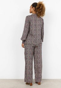 Dvou-dílný outfit s květinovým vzorem zahrnující dlouhé rukávy a široké kalhoty v odstínech fialové, krémové a zelené. Měkká, texturovaná tkanina.