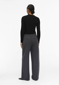 Black ribbed long-sleeve top paired with high-waisted, wide-leg gray trousers. Trousers feature an elastic waistband and side pockets.