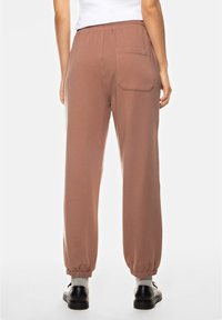 Bruine katoenen joggers met een elastische tailleband en manchetten, met een achterzak. De stof lijkt zacht met een gladde textuur.