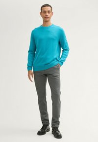 Turquoise trui met een ronde hals, gecombineerd met grijze slim-fit broek en zwarte veterschoenen. Eenvoudig en strak ontwerp.