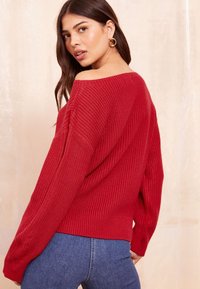 Pulover tricotat roșu, cu croială lejeră, design off-the-shoulder și textură canelată. Asortat cu blugi din denim albastru.