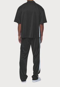 Zwart sportief setje met een top met korte mouwen en losse broek. Voorzien van lichtblauwe zijstrepen en een gladde, lichtgewicht stoftextuur.