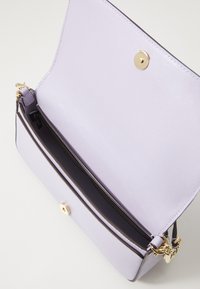 Lilac handbag with a textured finish, gold hardware, and a magnetic snap closure. Interior features are dark, with space for essentials.