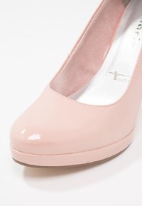 Chaussure pour femme à talon haut, bout fermé, rose pâle brillante, avec un avant arrondi et une finition lisse, vue en gros plan sous un angle.