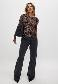 Leopard-print long-sleeve top, black high-waisted flared jeans, and a black shoulder bag. Black pointy-toed heels, smooth textures.