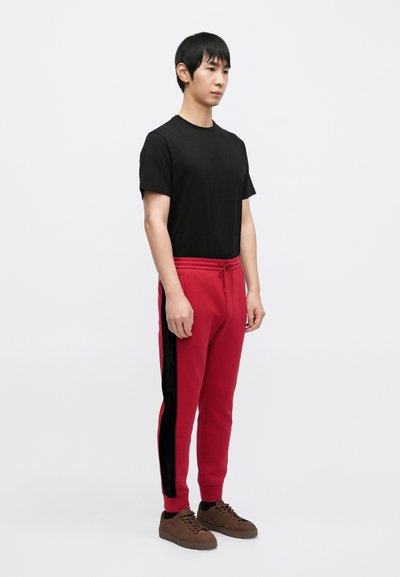 Punaiset collegehousut, joissa mustat sivuraidat, kapeahko leikkaus ja joustava vyötärönauha. Yhdistetty yksiväriseen mustaan lyhythihaiseen paitaan ja ruskeisiin lenkkareihin.