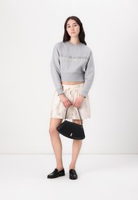 Grijze cropped sweater met het logo "ALLSAINTS", crèmekleurige rok met bloemenpatroon, zwarte gestructureerde handtas en zwarte schoenen.