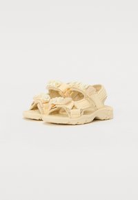 Des sandales beige clair présentent deux sangles réglables avec des accents texturés. La semelle en caoutchouc à crampons offre traction et stabilité.