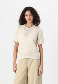 Beige gebreid sweater met korte mouwen, ronde halslijn en een gestructureerd patroon. Gepaard met lichtbruine wijde broek.