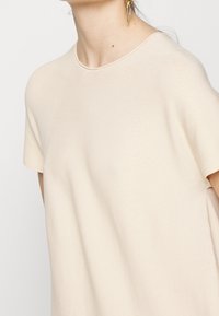 Top beige a maniche corte con una texture liscia e scollatura rotonda, caratterizzato da un leggero rigaggio e una vestibilità comoda.