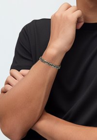 Silver-tone metal chain bracelet featuring interlinked flat segments, worn on a wrist, paired with a black short-sleeve shirt.