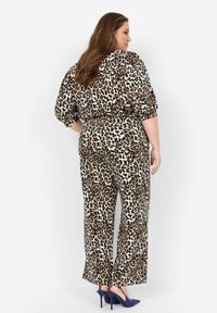 Leopardenmuster-Overall aus leichtem Stoff mit lockerer Passform, schmal zulaufenden Beinen und kurzen gepufften Ärmeln, kombiniert mit blauen High Heels.