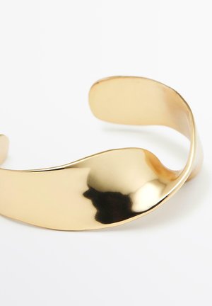 Metallcuffarmband i guldfärgad ton med en mjuk, vågig design och polerad yta. Har en flexibel, öppen form för enkel användning.