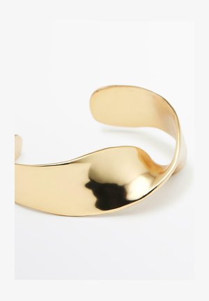 Metallcuffarmband i guldfärgad ton med en mjuk, vågig design och polerad yta. Har en flexibel, öppen form för enkel användning.