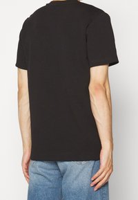 Svart bomullströja med korta ärmar, rund halsringning och enkel design. Bakifrån syns sömlös sömnad och en avslappnad passform. Bärs tillsammans med blå denimjeans.