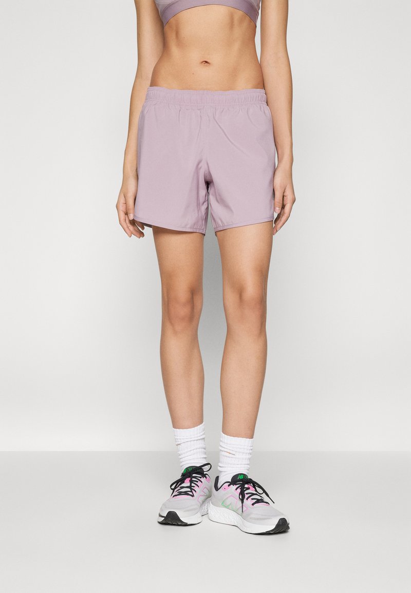 Shorts de sport lilas en matériau léger, avec une taille élastique et une coupe décontractée. Portés avec des chaussettes blanches et des chaussures de sport.