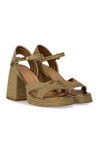 Χρυσές πλεχτές γόβες με ψηλό τακούνι, που διαθέτουν ένα φαρδύ λουρί στον αντίχειρα και λουρί στον αστράγαλο, με ανάγλυφο σφήνα τακούνι με ριγέ σχέδιο.