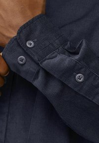 Camicia in corduroy blu navy con maniche, caratterizzata da un motivo testurizzato, due bottoni scuri al polso e una finitura in tessuto liscia.