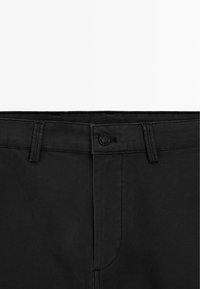 Zwarte katoenen broek met rechte snit, knoopsluiting en een tailleband met lussen. De stof heeft een gladde textuur met subtiele stikdetails.