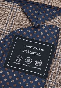 Teksturowana brązowa tkanina z granatowym, wzorzystym podszewką, na którym znajdują się małe motywy kwiatowe. Czarna metka z instrukcjami pielęgnacji i nazwą marki.