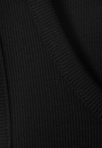 Crna rebrasta tkanina s teksturiranom površinom. Rubovi prikazuju uredan detalj šivanja, naglašavajući rastezljivost i strukturu materijala.