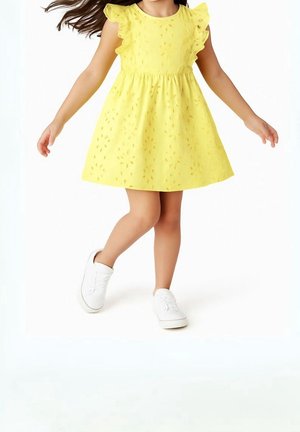 Vestido de algodón amarillo con cortes en forma de flores, mangas acampanadas con volantes y cintura elástica. Combinado con zapatillas blancas.